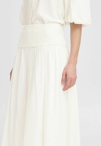 Jupe blanche fluide en tissu léger. Comprend une taille smockée et un design à volants et étagé pour ajouter texture et mouvement.