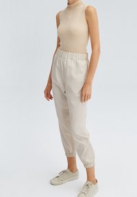 Beige geribde mouwloze top gecombineerd met beige joggerbroek met elastische taille, met gathered enkels. Het model draagt lichte sneakers.