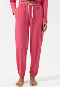 Roze loungebroeken van zacht materiaal met een elastische tailleband, verstelbaar trekkoord, zijzakken en taps toelopende boorden.