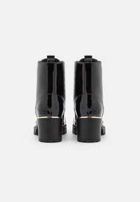 Czarne lakierowane botki za kostkę z okrągłym noskiem, średnim słupkowym obcasem i złotym akcentem przy obcasie, prezentujące gładką i błyszczącą fakturę.