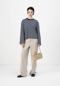 Camiseta de manga larga a rayas en azul marino y blanco, pantalones beige de pierna ancha, zapatos negros sin cordones y un pequeño bolso de mano color tostado. Materiales suaves, ajuste relajado.
