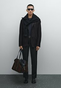 Black tailored blazer over a navy top, paired with black trousers. Accessories include black sunglasses and a brown suede bag with leather accents.