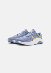 Zapatillas deportivas de color azul claro con una parte superior de malla texturizada, entresuela blanca y un acento en forma de swoosh amarillo en el costado. Punta redondeada y suela resistente.