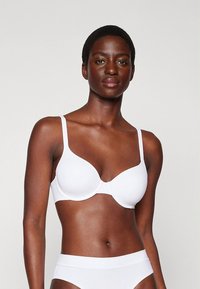 Soutien-gorge blanc légèrement rembourré avec bretelles ajustables. Présente une texture lisse et un design simple, offrant un maintien confortable.