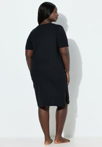 Vestito nero a maniche corte in tessuto morbido, con scollo rotondo e spacchi laterali sull'orlo per facilitare il movimento.