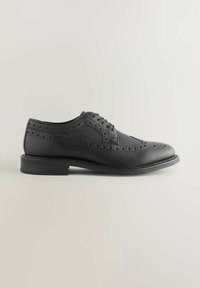 Chaussure oxford en cuir noir avec une finition texturée, des détails perforés le long des bords et une semelle basse et plate. Design classique moderne.