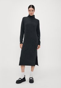 Mørk grå montering kjole med lange ermer, midt på leggen, sideåpning og ribbede mansjetter. Modellen har på klumpete svarte platå sko og hvite sokker.