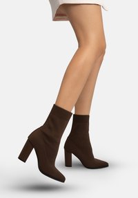 Braune gestrickte Stiefeletten mit Blockabsatz und spitzer Zehenpartie. Dehnbares Obermaterial mit geripptem Detail am Schaftbund. Vielseitig kombinierbar zu verschiedenen Outfits.