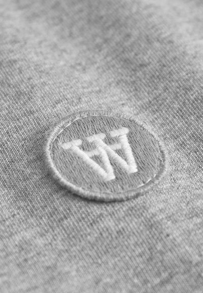 Grey fabric featuring a circular embroidered logo with the letters "W" in white. The texture is smooth with a subtle heather pattern.