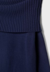 Granatowy sweter dzianinowy z prążkowanym kołnierzem. Posiada gładką teksturę i luźny krój, podkreślający komfort i dopasowanie.