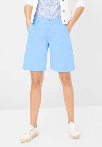 Lichtblauwe katoenen shorts met een knoopsluiting, zijzakken en een rechte snit, gecombineerd met witte canvas sneakers.