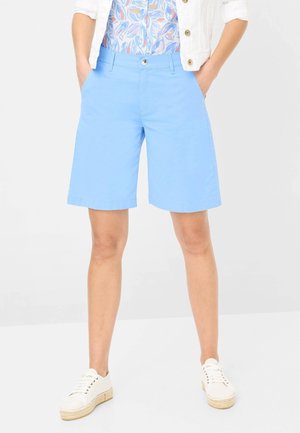 Shorts en coton bleu clair avec une fermeture à bouton, des poches latérales et une coupe droite, associés à des baskets en toile blanches.