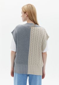 Gilet a maglia con un design a blocchi di colore che presenta tonalità di grigio e beige. Le trame includono modelli a coste e a trecce.