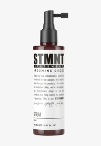 Bärnstensfärgad flaska med svart pumpdispensör. Fetstilad text på etiketten lyder "STMNT GROOMING GOODS" med "SERUM" under. Ren, modern design.
