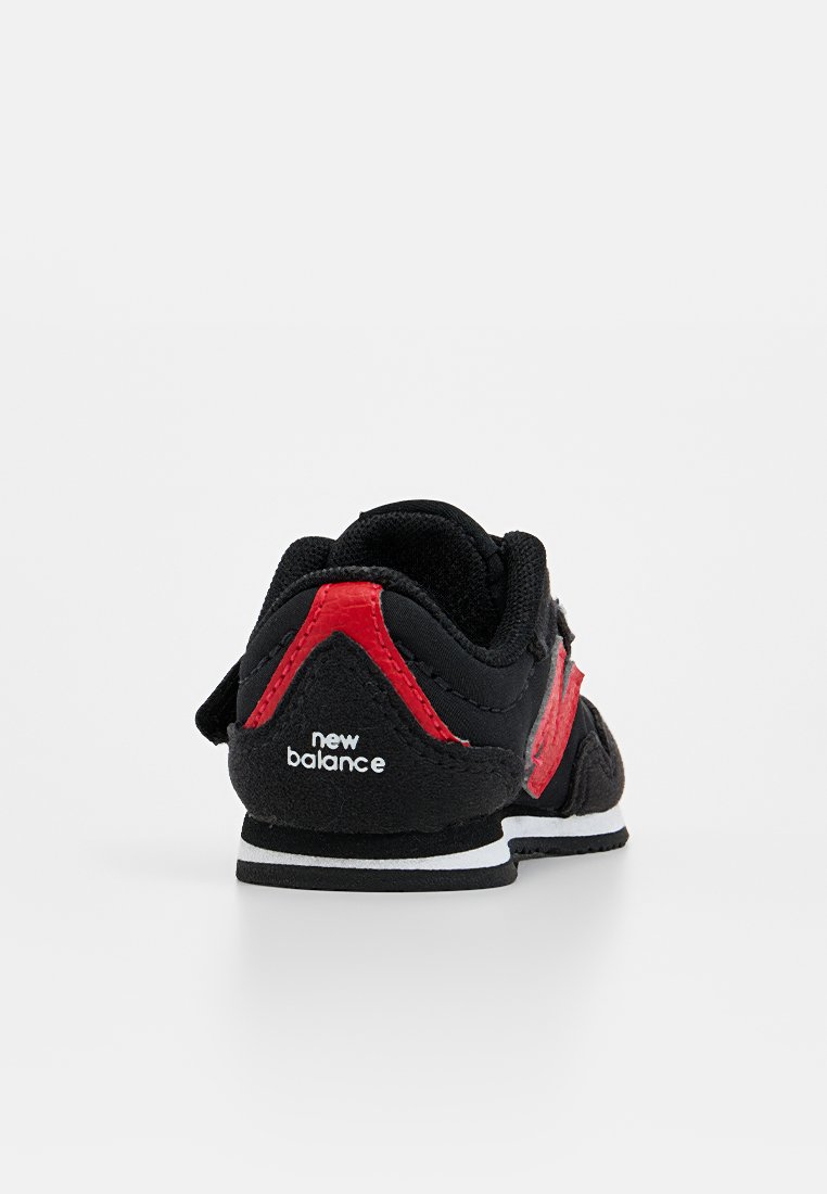 Baskets noires et rouges avec une tige en daim et en maille, arborant un logo "N" proéminent, un col rembourré et une semelle blanche avec des accents noirs.