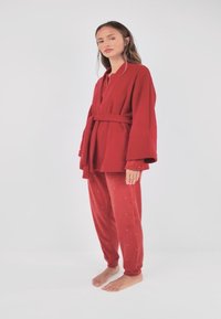 Ensemble lounge rouge composé d'une robe ceinturée à manches longues et d'un pantalon assorti avec de petites ornements dispersées. Texture douce et veloutée.