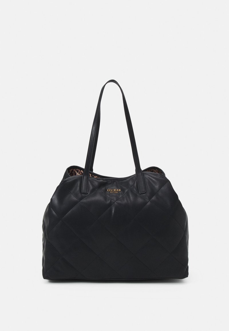 Sac à épaule noir matelassé avec longues anses, petit logo doré Guess centré près du haut, et doublure intérieure imprimée léopard visible.