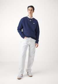 Marinblå sweatshirt med logotyp, vita byxor och sneakers med orangea accenter. Enkel design, avslappnad passform och mjuk textur.