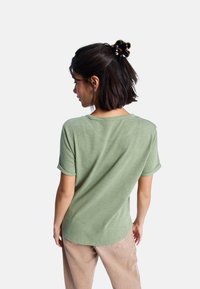 T-shirt vert clair à manches courtes avec un col rond et des manches roulées, associé à un pantalon beige. Tissu doux et coupe décontractée.