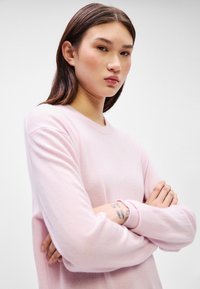 Ανοιχτό ροζ πουλόβερ με στρογγυλή λαιμόκοψη και μακριά μανίκια. Μαλακή υφή και ριπές στον καρπό. Απλός σχεδιασμός χωρίς ορατά σχέδια ή λεπτομέρειες.