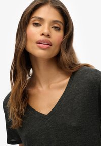 Dunkelgraues V-Ausschnitt-T-Shirt aus strukturiertem Stoff mit helleren Farbpartikeln. Verfügt über kurze Ärmel und ein dezentes Logo-Detail.