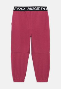 Różowe spodnie sportowe wykonane z miękkiego materiału, z czarnym pasem w talii z logo "PRO NIKE", slim fit i zwężanymi mankietami.