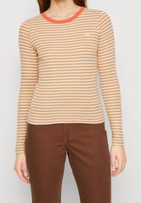Langärmliges gestreiftes Oberteil in Orange- und Beigetönen, runder Halsausschnitt und dezentes Levi's-Logo. Der Stoff hat eine glatte Textur.
