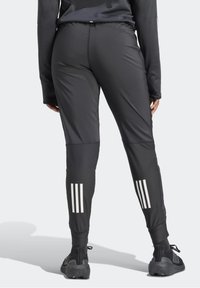 Zwarte sportbroek met een aansluitend ontwerp, voorzien van drie witte verticale strepen op de onderbenen en een panel van textuurstof.