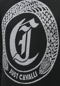 Pulover tricotat negru cu un logo circular proeminent gri, pe care scrie "JUST CAVALLI", și modele grafice intricate integrate în design.