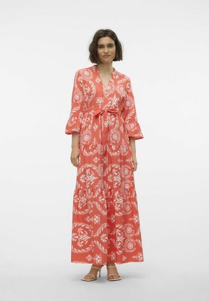 Robe maxi corail avec des motifs floraux blancs, présentant un col en V, des manches évasées et une taille à nouer. Le tissu est léger et fluide.