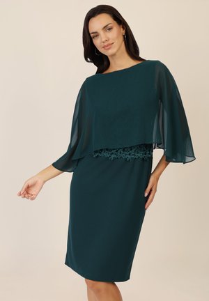 Teeled Kleid mit einem geschichteten Chiffon-Cape und Spitzensaum an der Taille. Der Stoff ist glatt mit einer enganliegenden Silhouette und reicht gerade über das Knie.