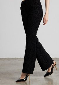 Pantalones negros de textura con un diseño de pierna acampanada, que presentan un sutil patrón floral. Combinados con mule de tacón alto negros y brillantes.