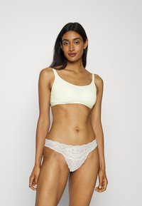 Sostén de color amarillo claro, sin costuras, con tirantes anchos y escote redondeado; tanga blanca con bordes festoneados y patrones de diamantes.