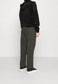 Giacca di velluto nero con cappuccio, caratterizzata da un motivo sottile. Abbinata a pantaloni larghi color verde oliva e sneakers nere chunky.