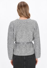 Grijze fuzzy trui met lange mouwen, voorzien van een ronde halslijn en een cinched taille met een grijze strikriem, gedragen over een donkere rok.