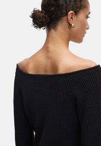 Schwarzer, gerippter, schulterfreier Pullover mit strukturiertem Strickmuster, langen Ärmeln und offener Halsgestaltung.