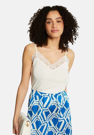 Camisola bianca con pizzo lungo il colletto, abbinata a una gonna blu e bianca con motivo geometrico. Modello a vestibilità morbida.