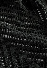 Schwarzer Strickstoff mit einem strukturierten, offenen Webmuster. Enthält diagonale Linien und kleine rechteckige Öffnungen im gesamten Stoff.