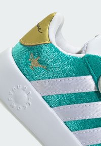 Tyrkysové textilné tenisky s bielymi pruhmi, zlatými detailmi na podpätku a štruktúrovaným povrchom. Obsahuje logo vyrazené na podrážke.