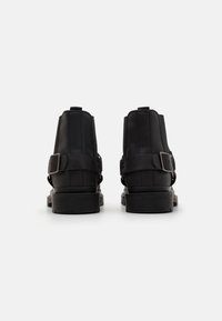 Botas de cuero negras hasta el tobillo con una textura suave, que presentan correas laterales dobles con hebillas y una suela de goma gruesa para mayor durabilidad.