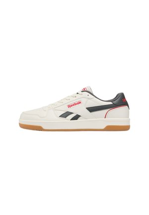 Zapatilla Reebok baja en color blanco hueso con rayas laterales negras, marca en rojo y suela de goma natural, vista desde el lado derecho.