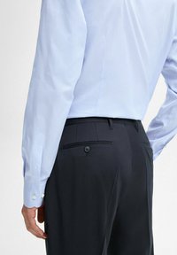 Light blue striped dress shirt with buttoned cuffs, paired with dark trousers featuring a back pocket and button closure.