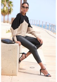 Schwarzer und beiger Strickpullover mit Fledermausärmeln, kombiniert mit enganliegenden, schwarzen Leggings und schwarzen, geschnürten Sandalen mit Absatz. Texturierte Clutch daneben.