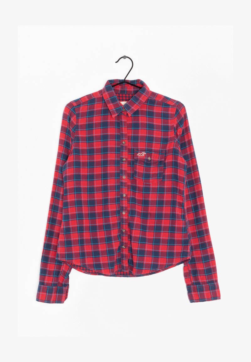 Camicia a maniche lunghe a quadri rossi e blu navy con colletto, chiusura con bottoni e taschino sul petto con un piccolo logo. Tessuto di cotone, leggermente testurizzato.
