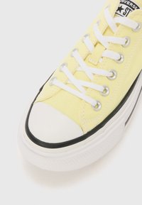Yellow canvas sneaker with white laces, rubber toe cap, and black sole trim. Features metallic eyelets and textured canvas surface.