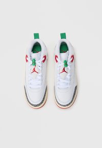 Białe sneakersy wykonane ze skóry i materiału siatkowego. Posiadają czerwone i zielone akcenty, czarną wzorzystą podeszwę oraz białe sznurowadła. Zielony uchwyt na pięcie.