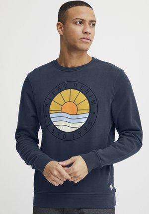 Navy sweatshirt with a round, multicolored graphic featuring a sun, waves, and text. Ribbed cuffs and hem, cotton blend material.