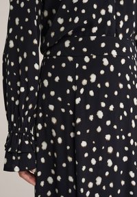 Melna auduma kleita ar baltu un brūnu plankumu rakstu. Piedurknes ar savāktām drapērijām un plata jostas vieta konstrukcijai. Mīksta tekstūra.