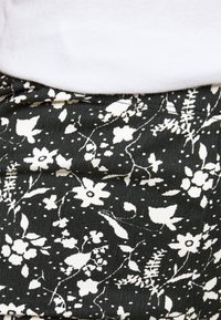 Blommönstrad kjol i svart och vitt. Har en ribbad struktur med olika blommor och blad i en spridd design. Elastisk midja synlig.