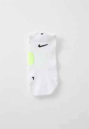Baltā sporta zeķe ar melno Nike logotipu, spilgti neona dzeltenu akcentu, ribotu tekstūru uz ķermeņa un melnu numuru "7" pie pēdas.